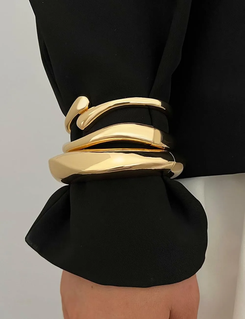 Close-up of chunky gold bangle bracelets on a black sleeve
