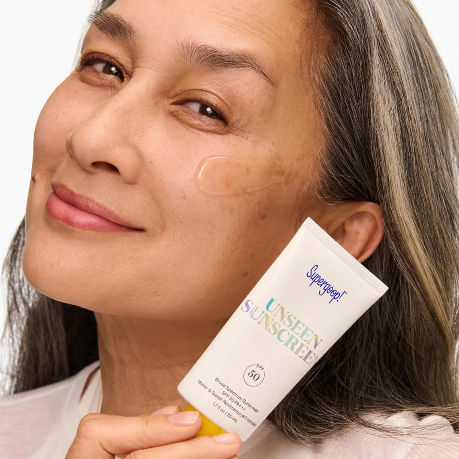Model holding Supergoop Unseen Sunscreen with clear gel on skin