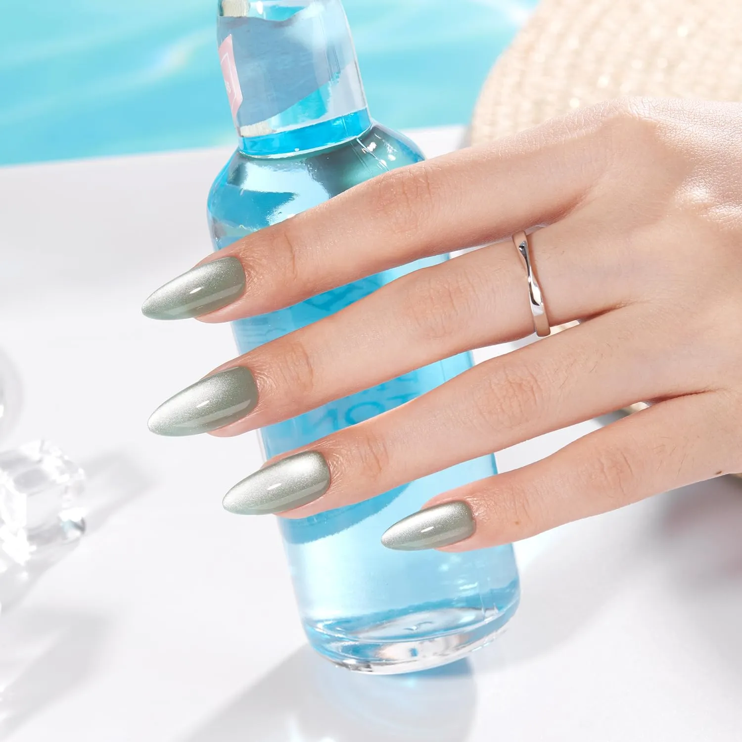 Hand wearing sage-green cat eye chrome almond nails near a blue bottle